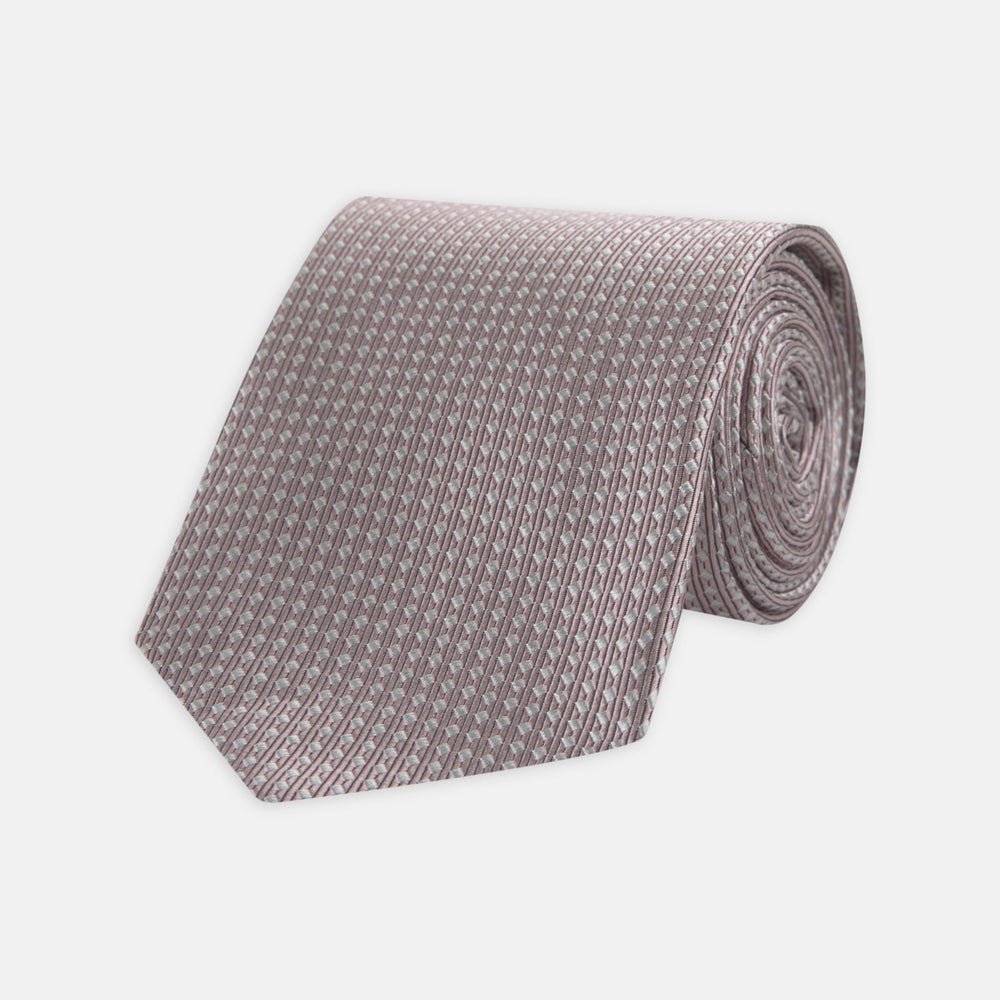 The Turnbull & Asser Rose and White Diamond Silk Tie, shown rolled on a white background, features a subtle diamond pattern—an elegant accessory to elevate any office shirt.