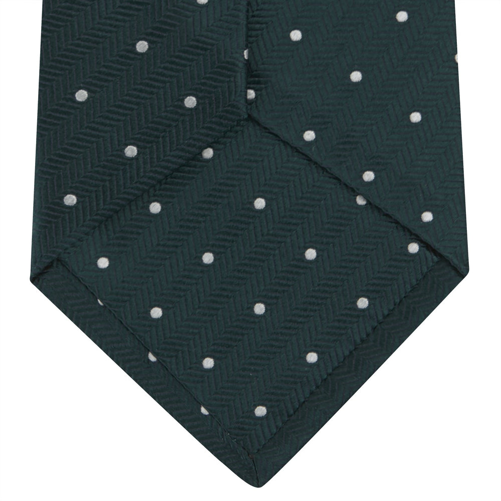 The Forest Green and White Small Spot Herringbone Silk Tie by Turnbull & Asser features a dark green woven herringbone pattern with small white spots, crafted from fine English silk and shown rolled up on a white background.