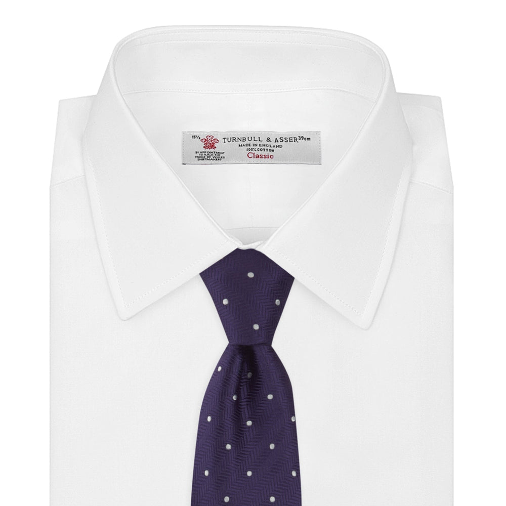 The Turnbull & Asser Plum and White Small Spot Herringbone Silk Tie is shown rolled up on a plain white background, featuring a classic silk herringbone weave in plum with small white spots.