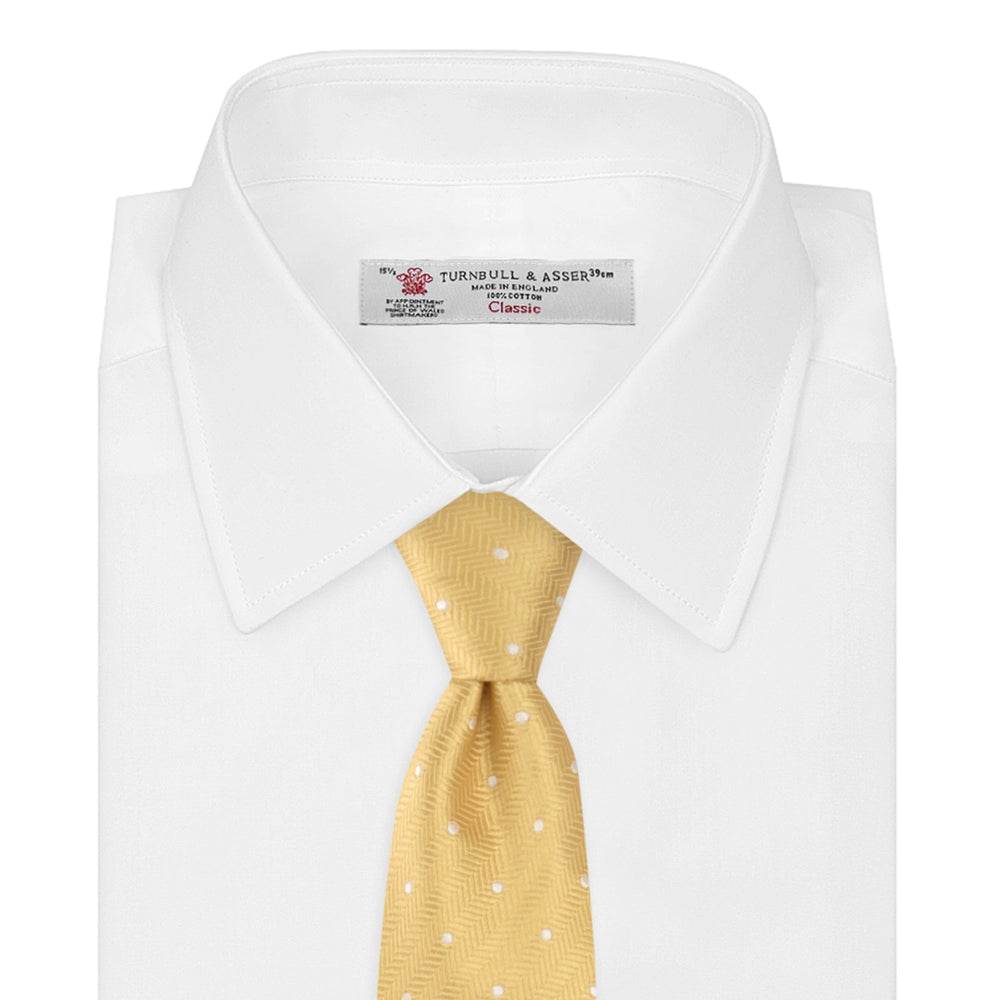 The Turnbull & Asser Gold and White Small Spot Herringbone Silk Tie is crafted from fine English silk, featuring a gold herringbone weave with white polka dots, and is shown rolled up on a white background.