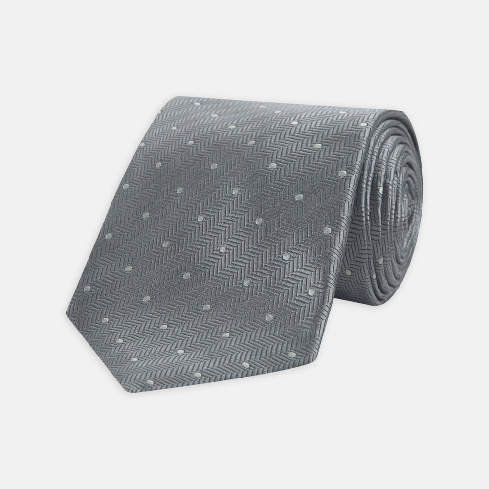 The Turnbull & Asser Grey and White Small Spot Herringbone Silk Tie, expertly woven from silk, is displayed rolled-up against a white background.