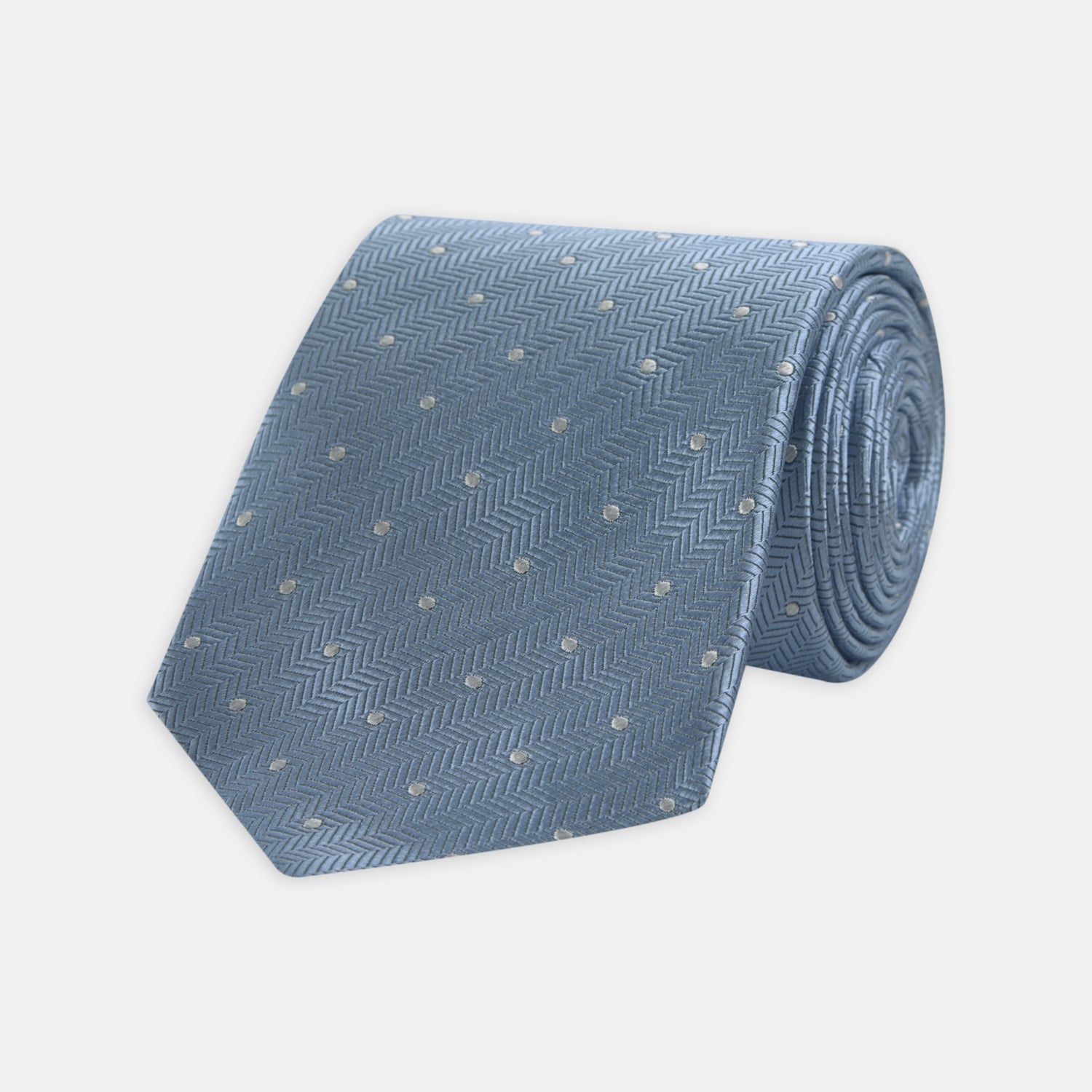 View 1 of product The Turnbull & Asser Ice Blue and White Small Spot Herringbone Silk Tie features a refined herringbone weave with subtle white spots, displayed elegantly against a plain white background.