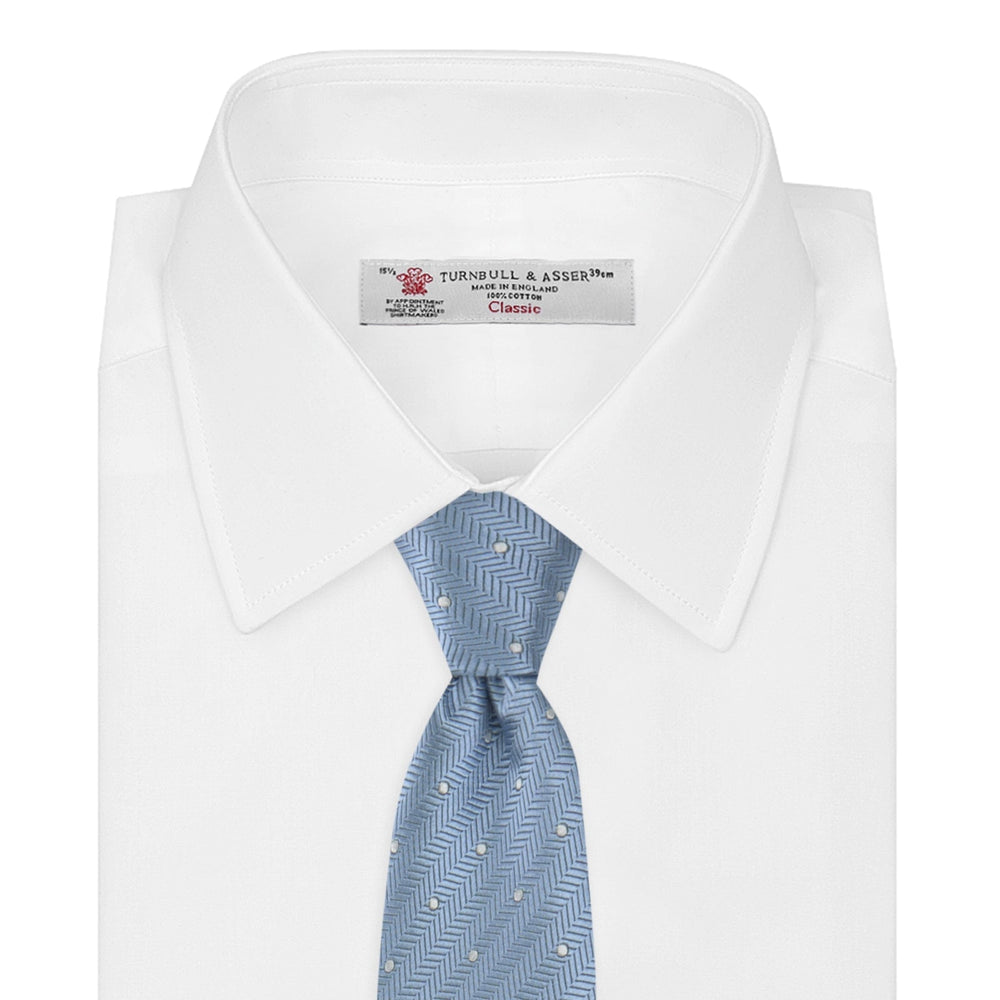 The Turnbull & Asser Ice Blue and White Small Spot Herringbone Silk Tie features a refined herringbone weave with subtle white spots, displayed elegantly against a plain white background.