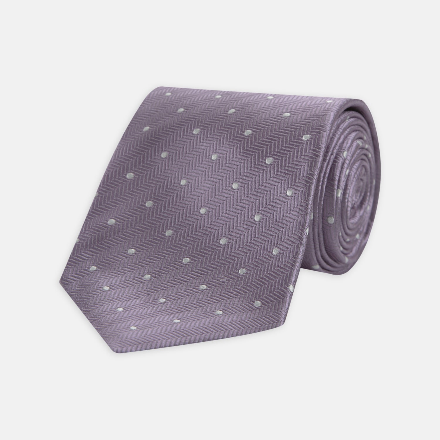 View 1 of product The Turnbull & Asser Lilac and White Small Spot Herringbone Silk Tie, crafted from fine English silk, is neatly rolled and displayed on a plain white background.
