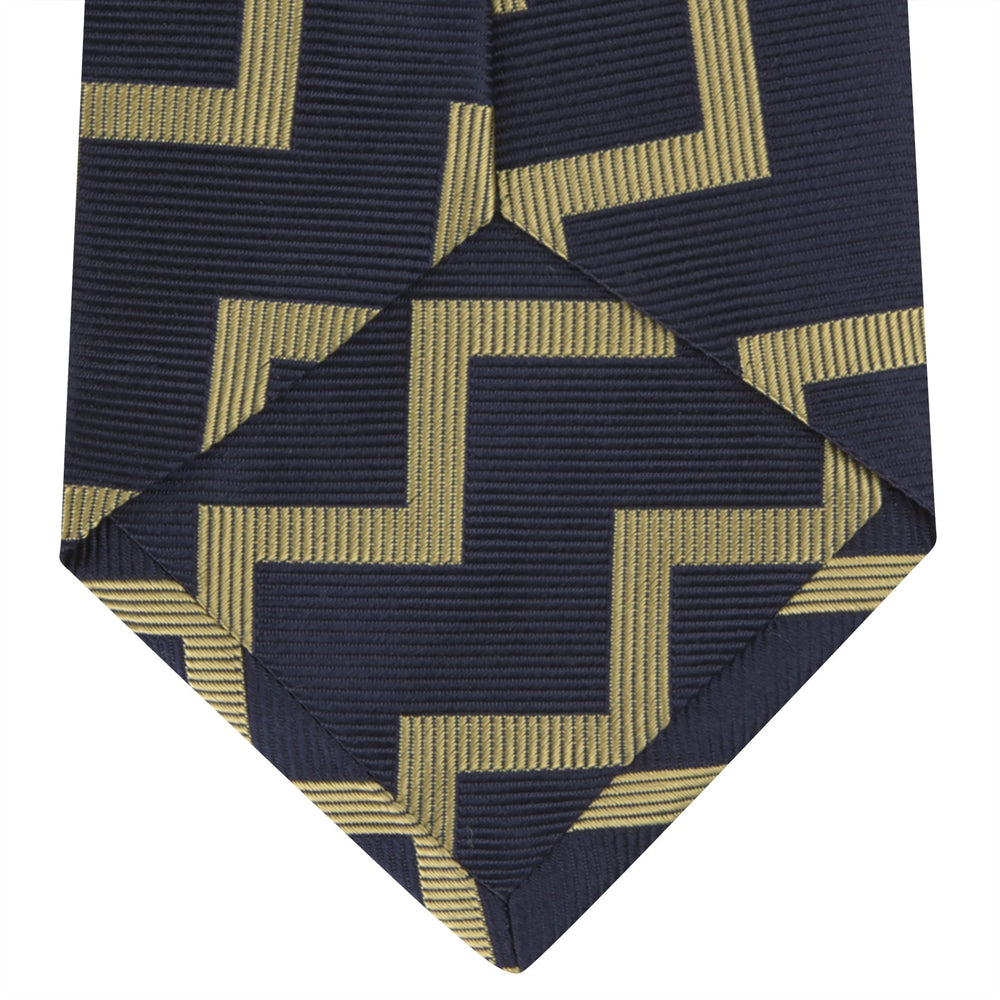 The Navy and Gold Striped Zigzag Silk Tie by Turnbull & Asser features a bold geometric pattern—an essential modern accessory shown rolled up with the pointed end forward on a white background.