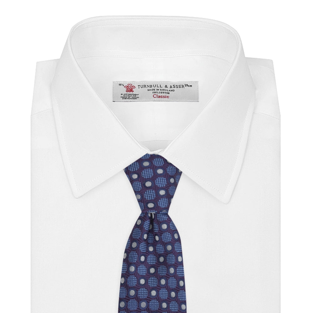 The Turnbull & Asser Plum and Blue Circle and Spot Silk Tie, shown rolled up on a white background, features a classic pattern—an elegant choice to complement any office shirt.