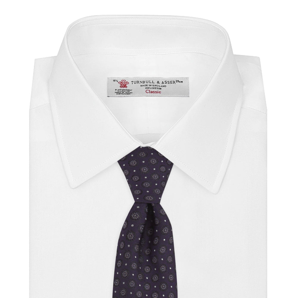 The Turnbull & Asser Plum Floral Spot Silk Tie features a rolled-up classic design with small, evenly spaced floral spots in lighter purple and white, ideal for office shirts and shown against a plain white background.