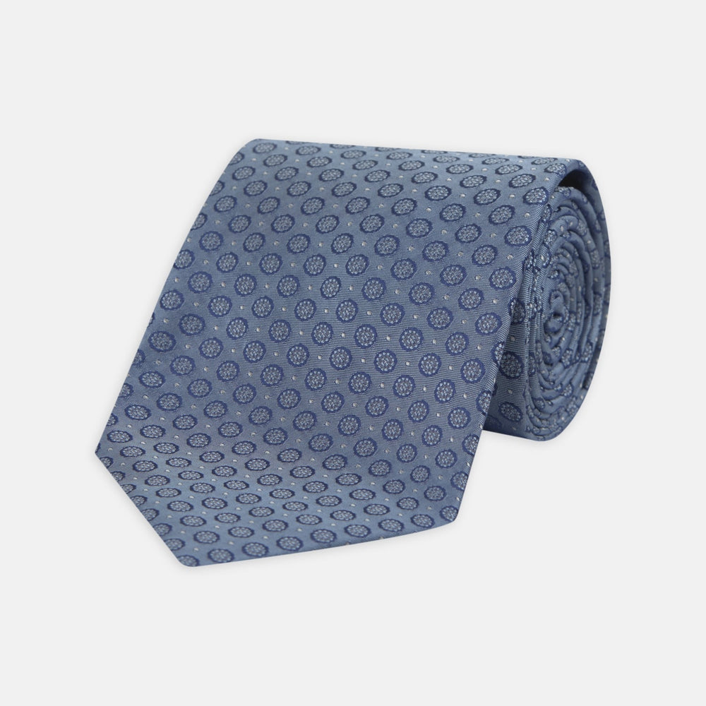 The Light Blue Floral Spot Silk Tie by Turnbull & Asser features a classic pattern in varied blue tones, rolled up on a white background—an ideal accessory to complement any office shirt.