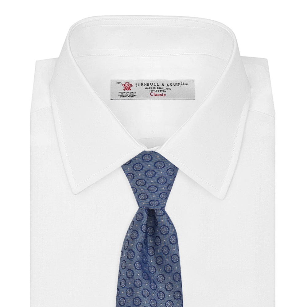 The Light Blue Floral Spot Silk Tie by Turnbull & Asser features a classic pattern in varied blue tones, rolled up on a white background—an ideal accessory to complement any office shirt.