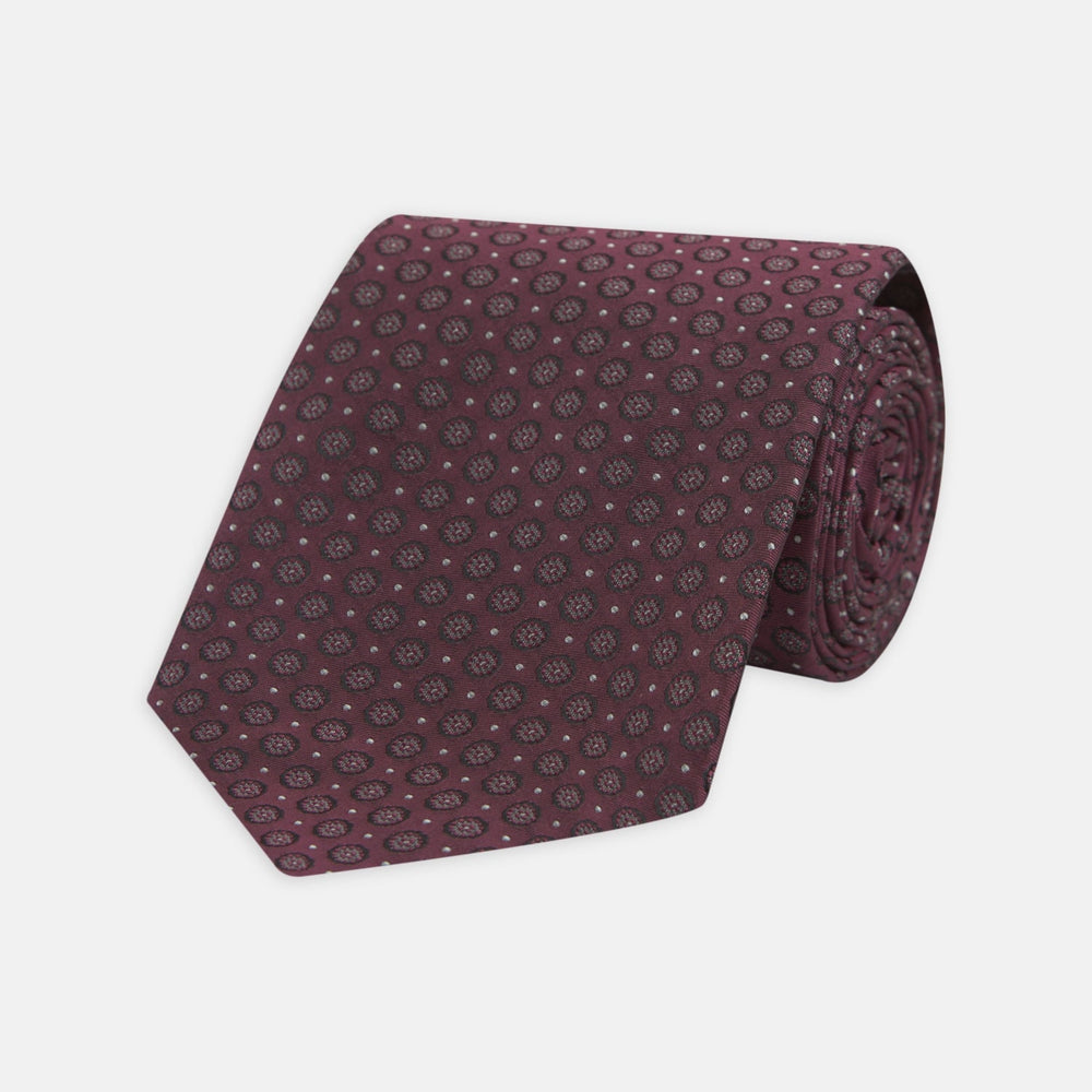 The Turnbull & Asser Wine Floral Spot Silk Tie features a rolled design with a gray and black circular pattern, perfect for the office. Displayed on a plain white background.