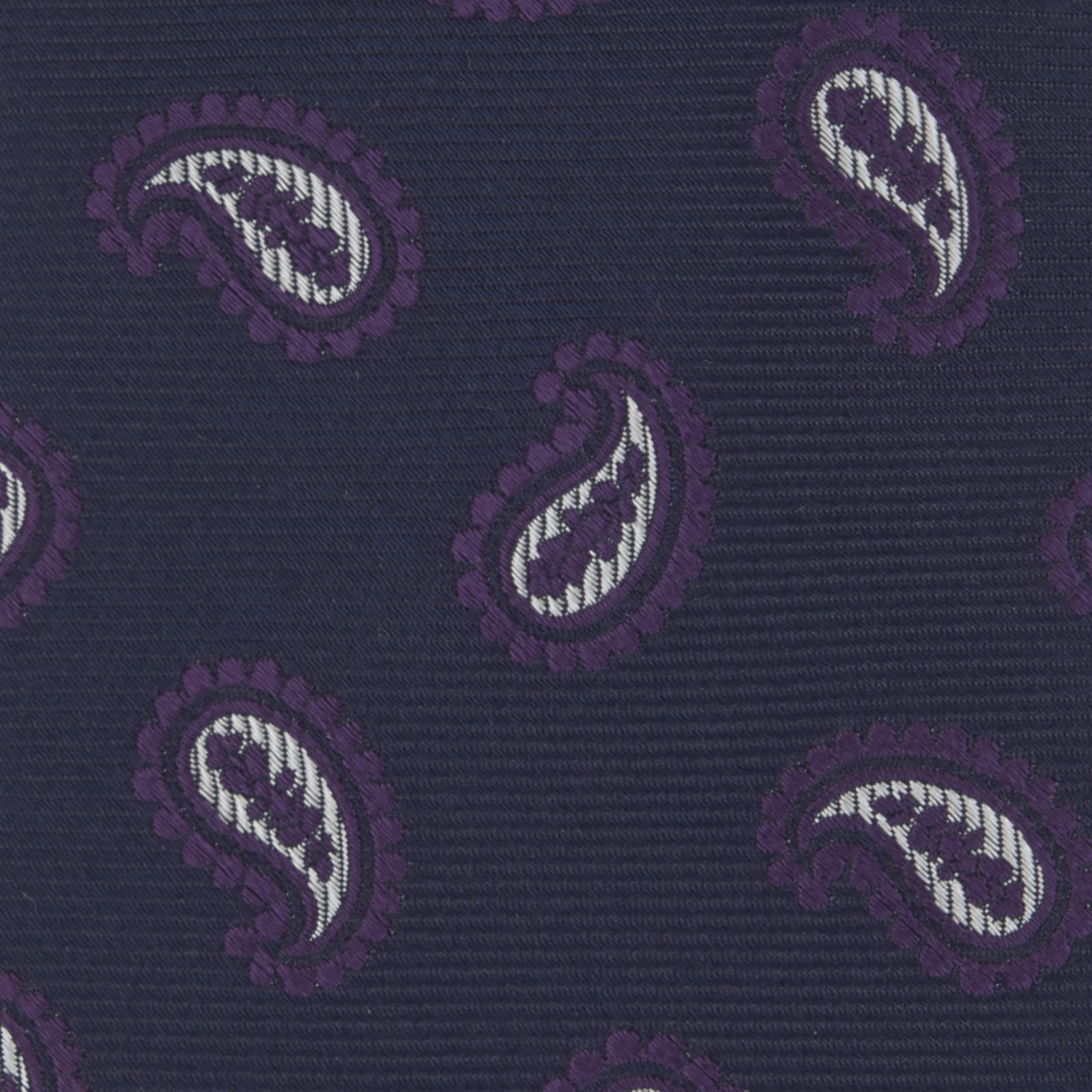 View 3 of product The Turnbull & Asser Navy and Plum Floating Paisley Silk Tie features a repeating purple and white paisley pattern, elegantly rolled up on a white background.