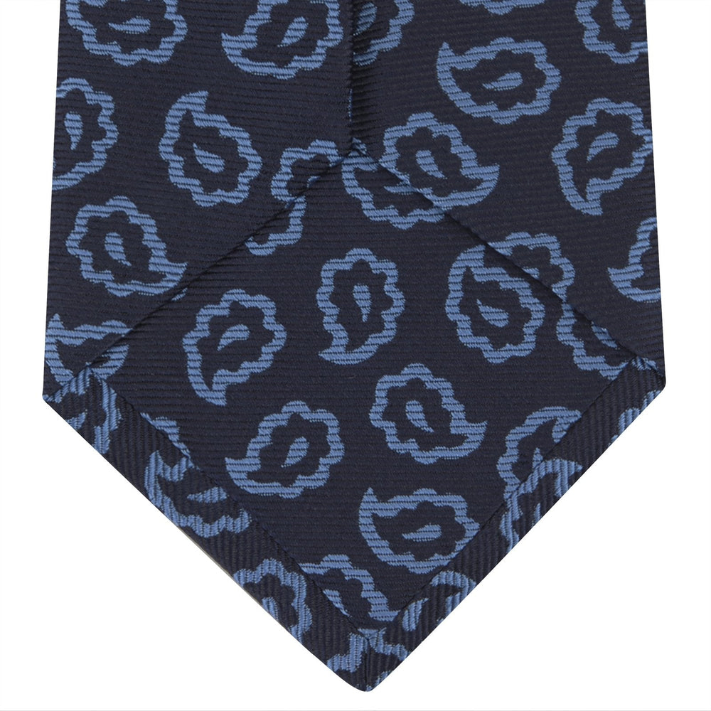 The Navy and Blue Petal Paisley Silk Tie by Turnbull & Asser features an abstract pattern of light blue paisley-like shapes, rolled up and displayed on a white background.