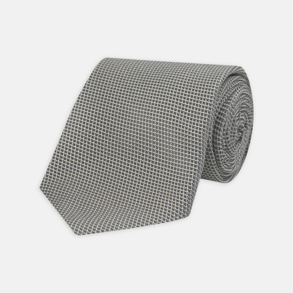 The Turnbull & Asser Light Grey Grenadine Silk Tie features a finely textured checkered pattern and superb dimensional stability, shown rolled up against a plain white background.