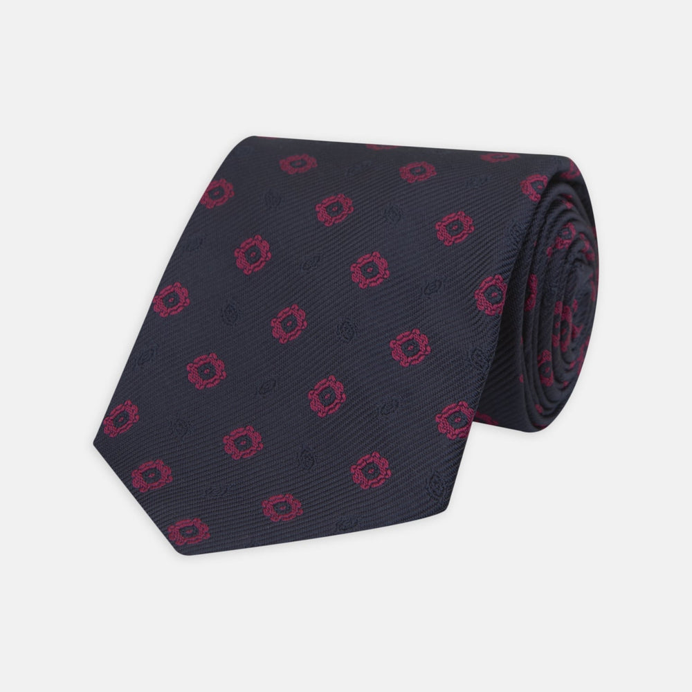 The Turnbull & Asser Navy and Dark Pink Emblem Spot Silk Tie features a classic pattern of small, evenly spaced emblems—ideal for complementing your favorite office shirt.