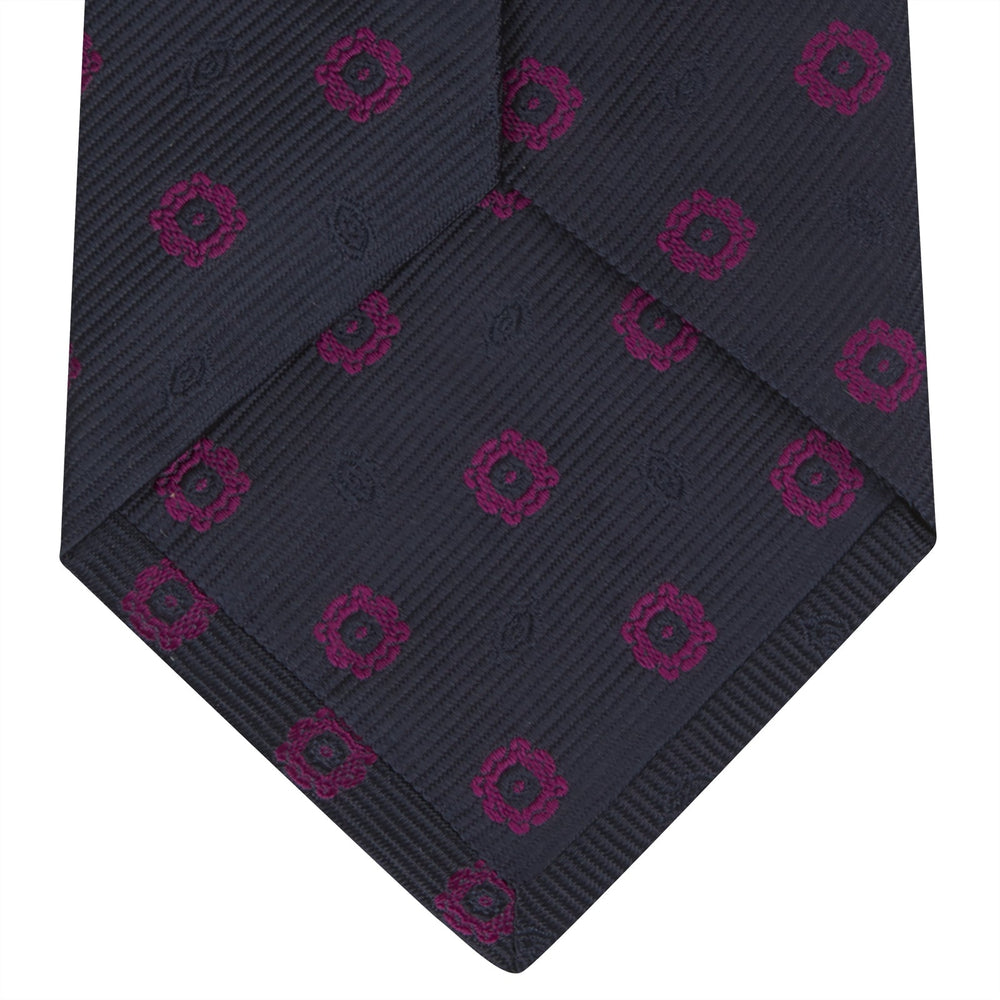 The Turnbull & Asser Navy and Dark Pink Emblem Spot Silk Tie features a classic pattern of small, evenly spaced emblems—ideal for complementing your favorite office shirt.