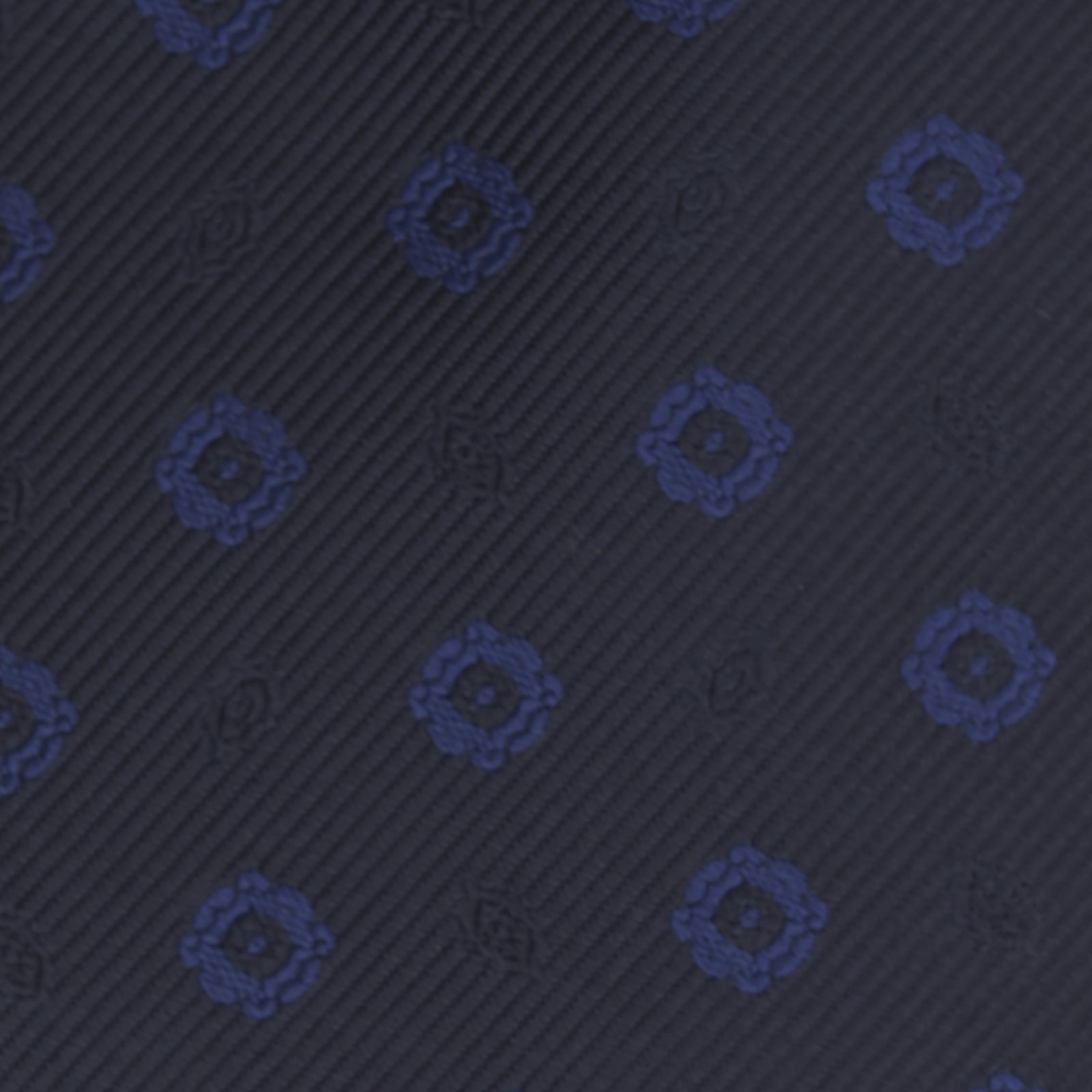 View 3 of product The Turnbull & Asser Navy and Blue Emblem Spot Silk Tie features a classic pattern of light blue motifs on navy silk, showcased rolled on a white background—a refined accessory for any office shirt.