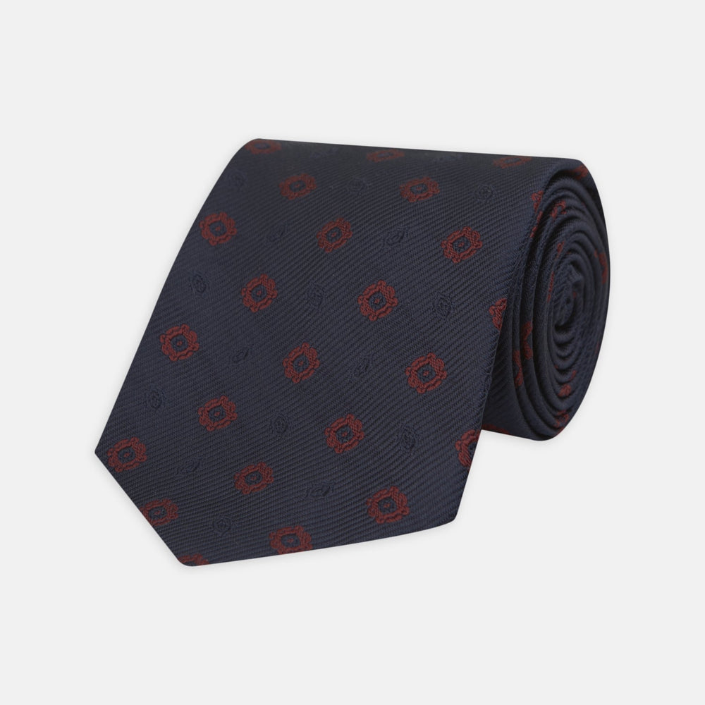 The Turnbull & Asser Navy and Burgundy Emblem Spot Silk Tie features a subtle textured pattern with small burgundy emblems on navy silk. Perfectly rolled with a pointed tip, it pairs well with any office shirt.