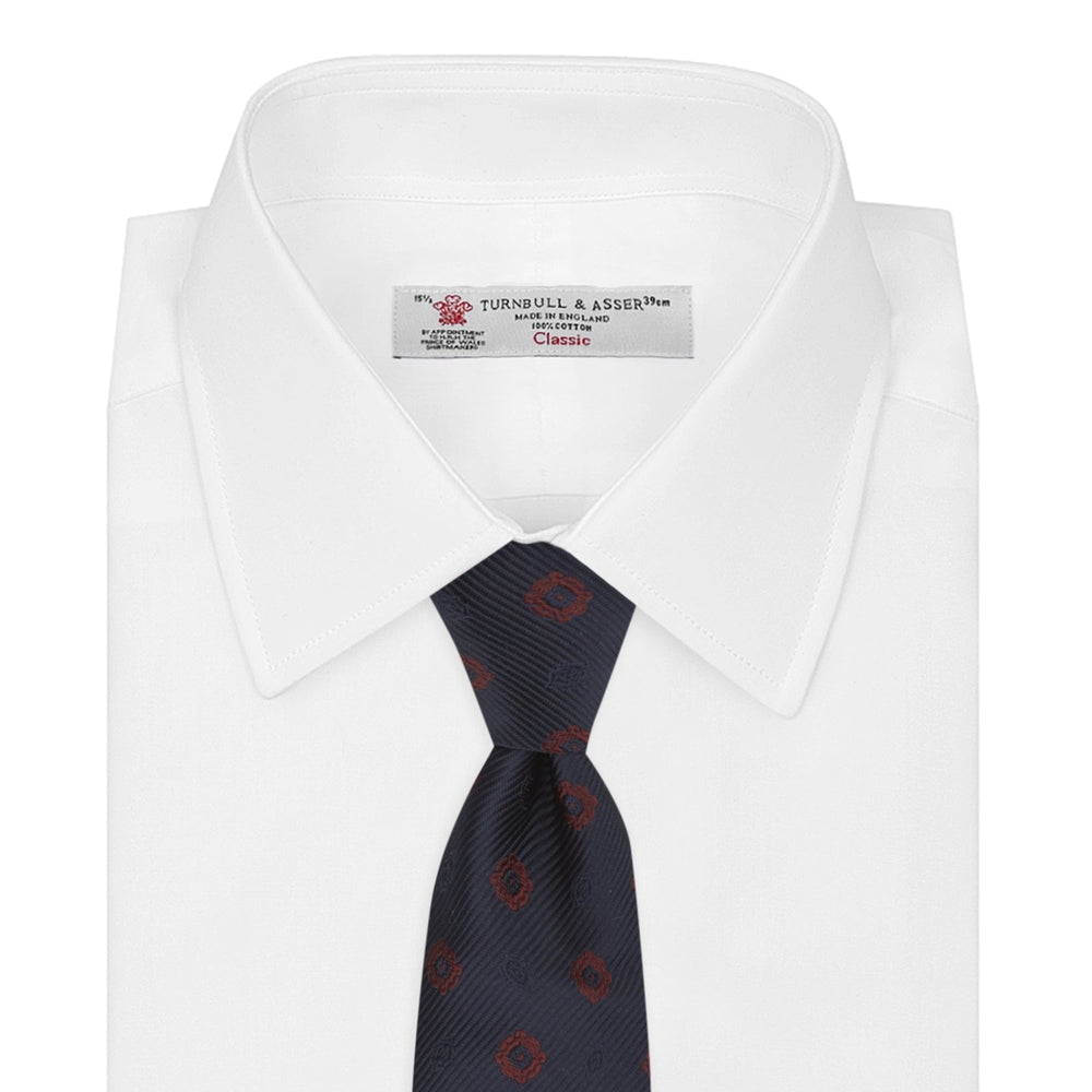 The Turnbull & Asser Navy and Burgundy Emblem Spot Silk Tie features a subtle textured pattern with small burgundy emblems on navy silk. Perfectly rolled with a pointed tip, it pairs well with any office shirt.