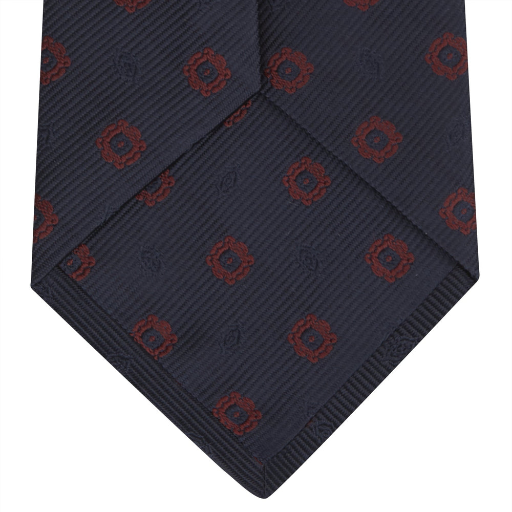 The Turnbull & Asser Navy and Burgundy Emblem Spot Silk Tie features a subtle textured pattern with small burgundy emblems on navy silk. Perfectly rolled with a pointed tip, it pairs well with any office shirt.