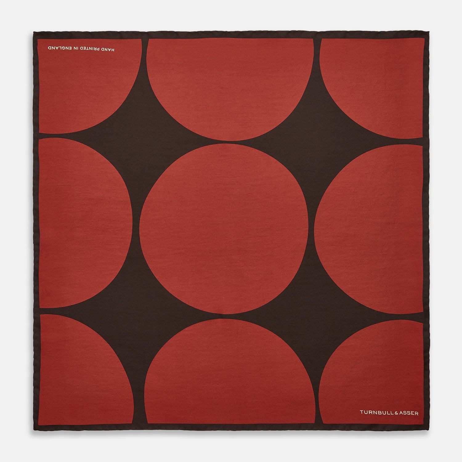 View 1 of product The DR. NO Red and Black Multi Spots Silk Pocket Square by Turnbull & Asser is handmade in England, featuring large red circles on black, with "Turnbull & Asser" and "Made in England" printed in white in the corners.