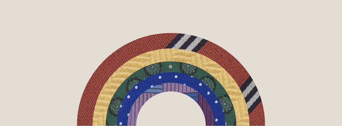 Illustration of a rainbow made from textured fabric bands in red, yellow, green, blue, and purple patterns, set against a light beige background.