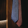 View 3 of product The Turnbull & Asser Die Another Day Stripe Silk Tie, as seen on James Bond, showcases a vibrant orange, red, and purple woven pattern, elegantly rolled and displayed against a white background.