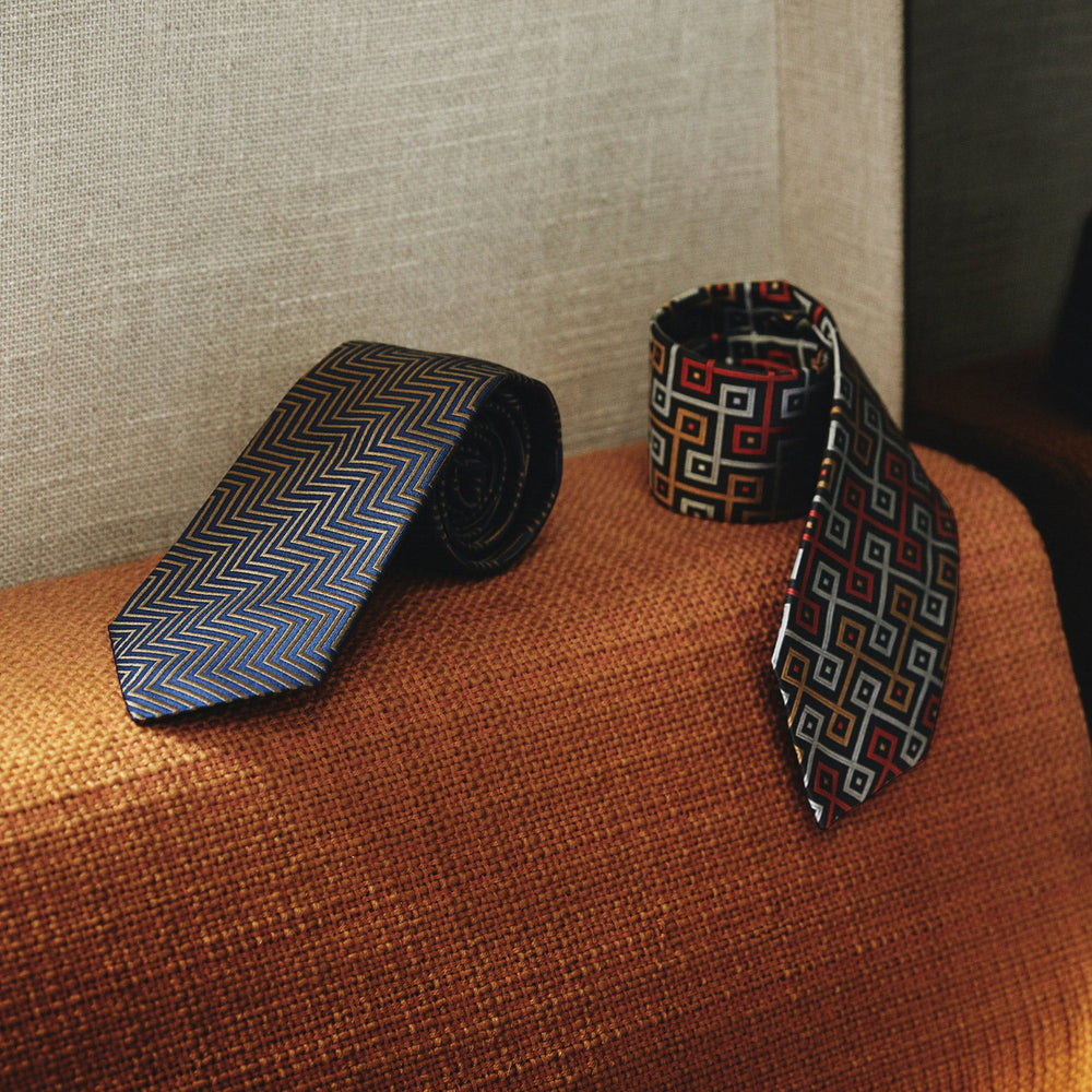 Turnbull & Asser's "The World Is Not Enough" Zig Zag Silk Tie, as seen on James Bond, features a bold navy blue and gold chevron design and is shown neatly rolled on a white background.