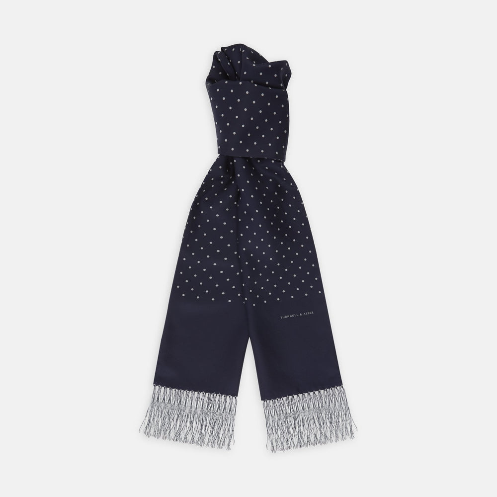 The Turnbull & Asser Navy and White Spotted Silk Scarf with Fringes, featuring small polka dots and grey fringe at both ends, is neatly folded and displayed on a plain white background.