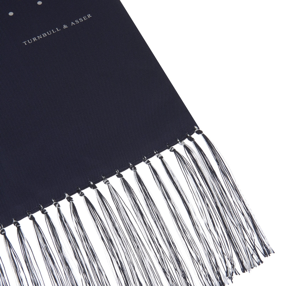 The Turnbull & Asser Navy and White Spotted Silk Scarf with Fringes, featuring small polka dots and grey fringe at both ends, is neatly folded and displayed on a plain white background.