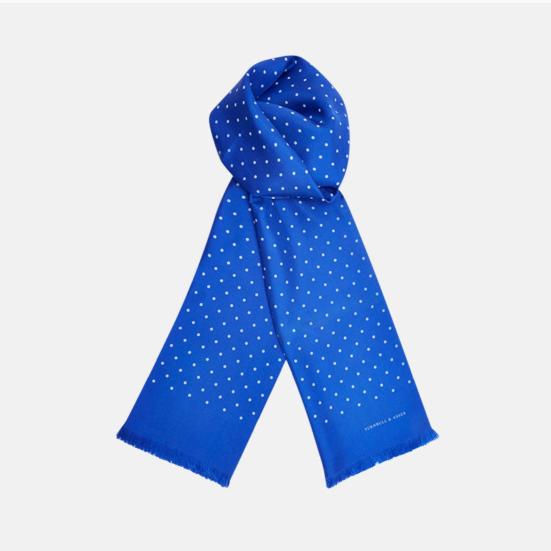 The Turnbull & Asser Royal Blue and White Spotted Silk Scarf features a soft silk fabric, short fringes at both ends, neatly folded center, and a hand-printed polka dot design for a distinctive, elegant look.