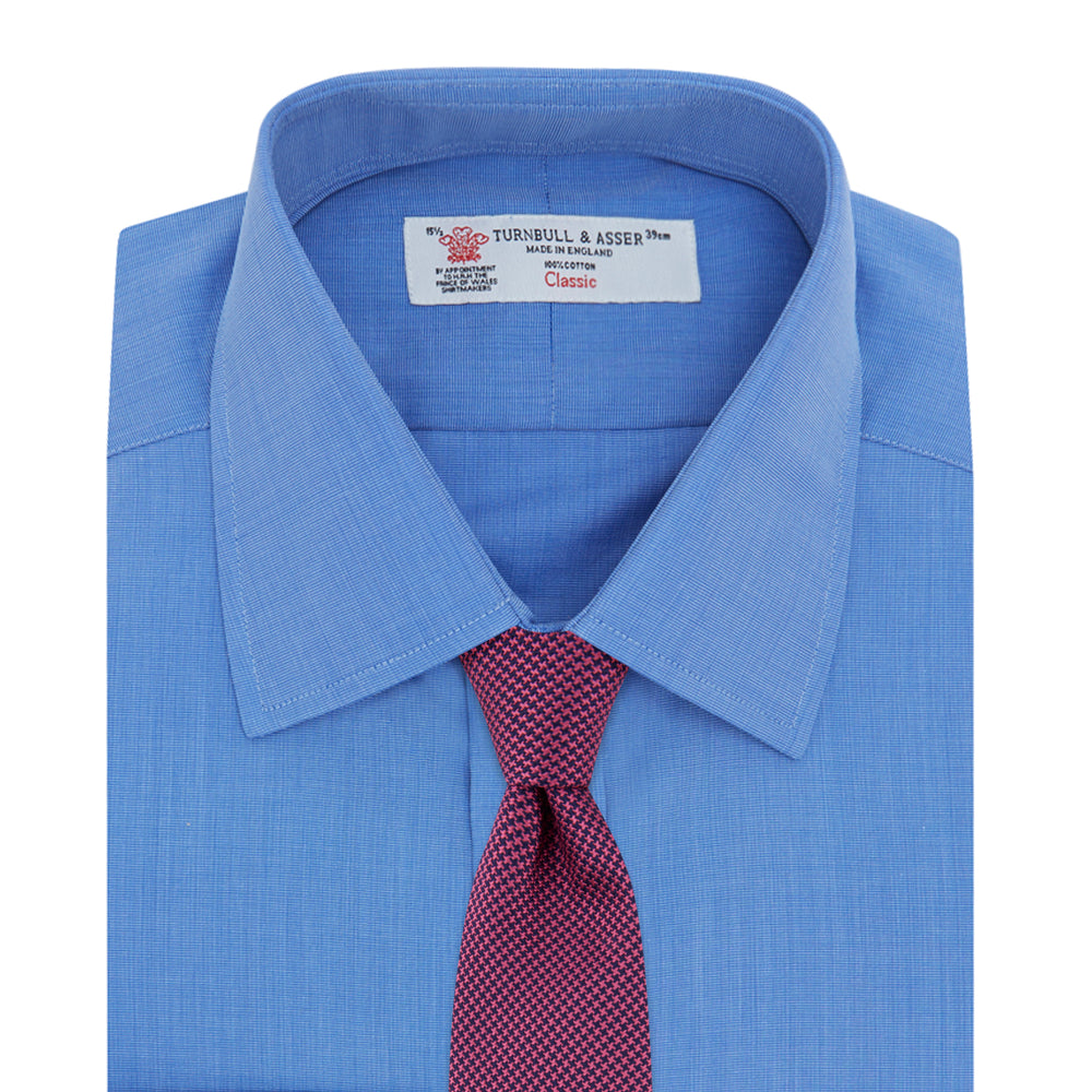 A neatly folded, dark blue end-on-end men's dress shirt by Turnbull & Asser, featuring a T&A collar and double cuffs, is displayed against a plain white background.