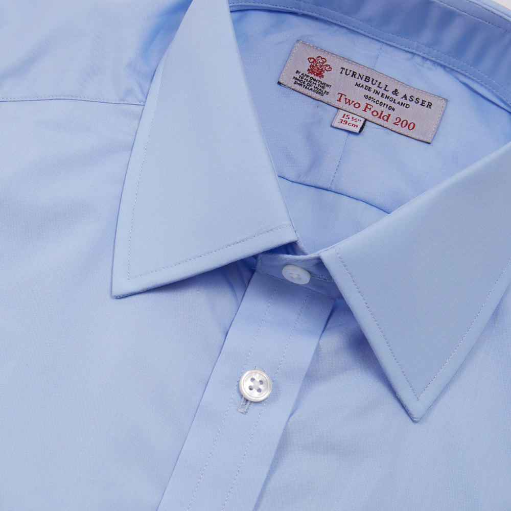 The Turnbull & Asser Two-Fold 200 Blue Cotton Shirt features a T&A collar, double cuffs, white buttons, and a visible label inside the collar, displayed neatly folded on a plain white background for superior breathability.