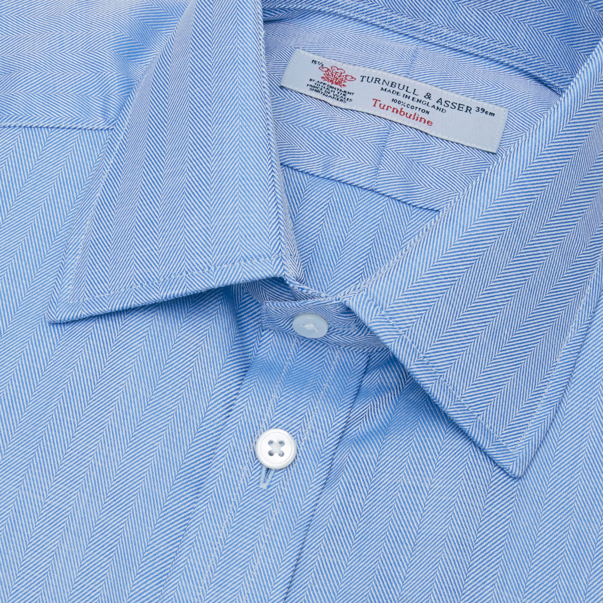 View 5 of product The Turnbull & Asser Blue Herringbone Superfine Cotton Shirt features a T&A collar and double cuffs—an essential for discerning gentlemen—shown folded on a plain white background.