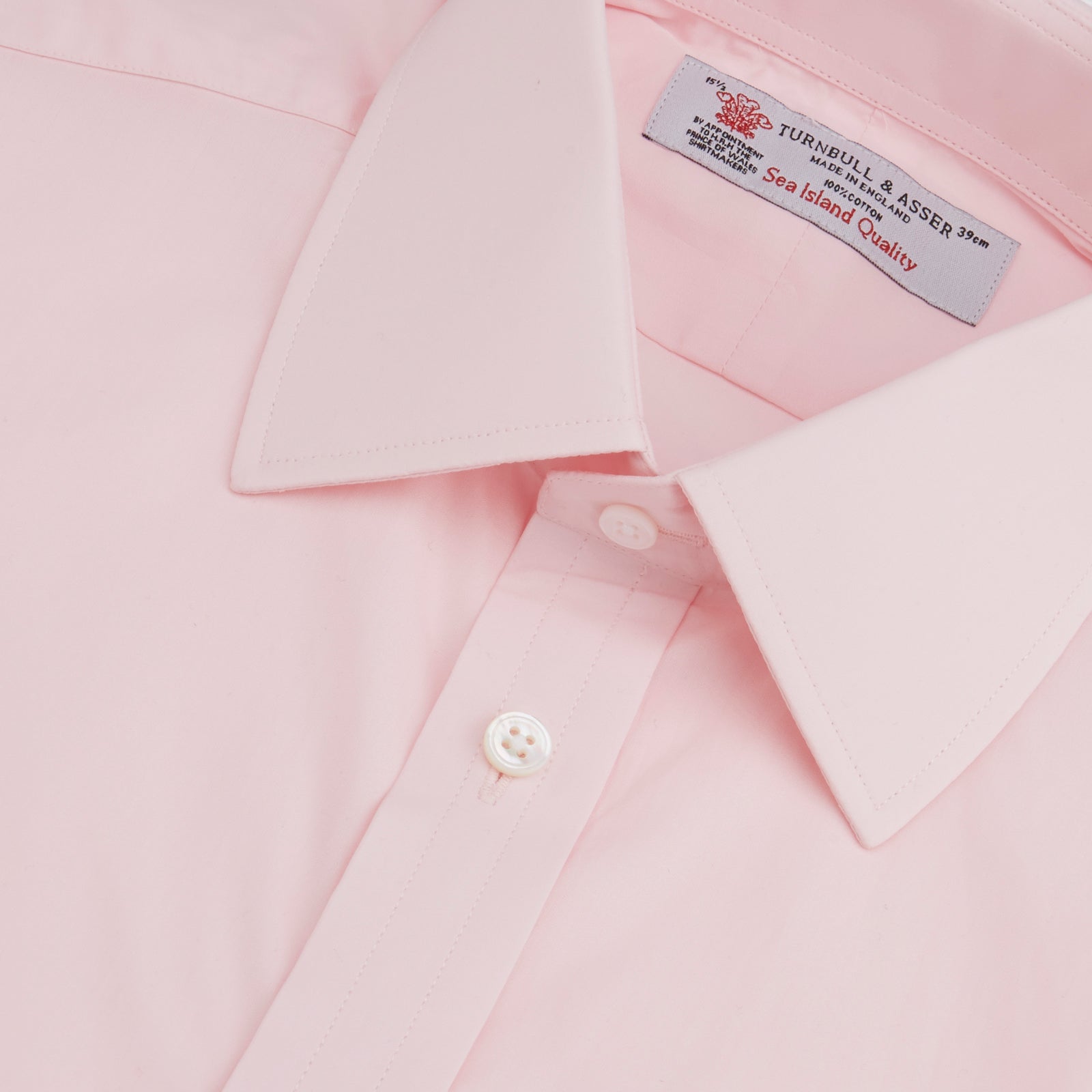 View 5 of product A slim black herringbone silk tie by Turnbull & Asser is paired with a neatly folded light pink long-sleeve dress shirt with a classic collar and white buttons, all displayed on a plain white background.