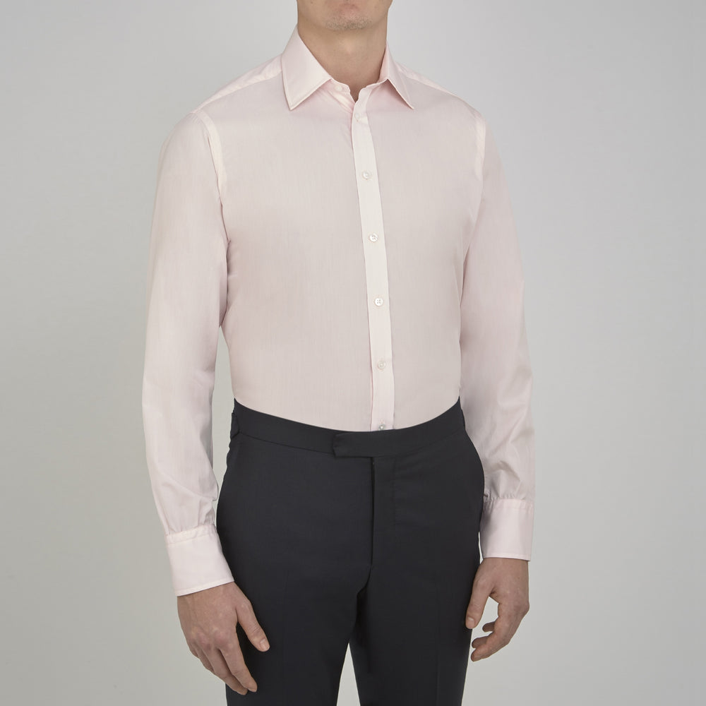 A slim black herringbone silk tie by Turnbull & Asser is paired with a neatly folded light pink long-sleeve dress shirt with a classic collar and white buttons, all displayed on a plain white background.