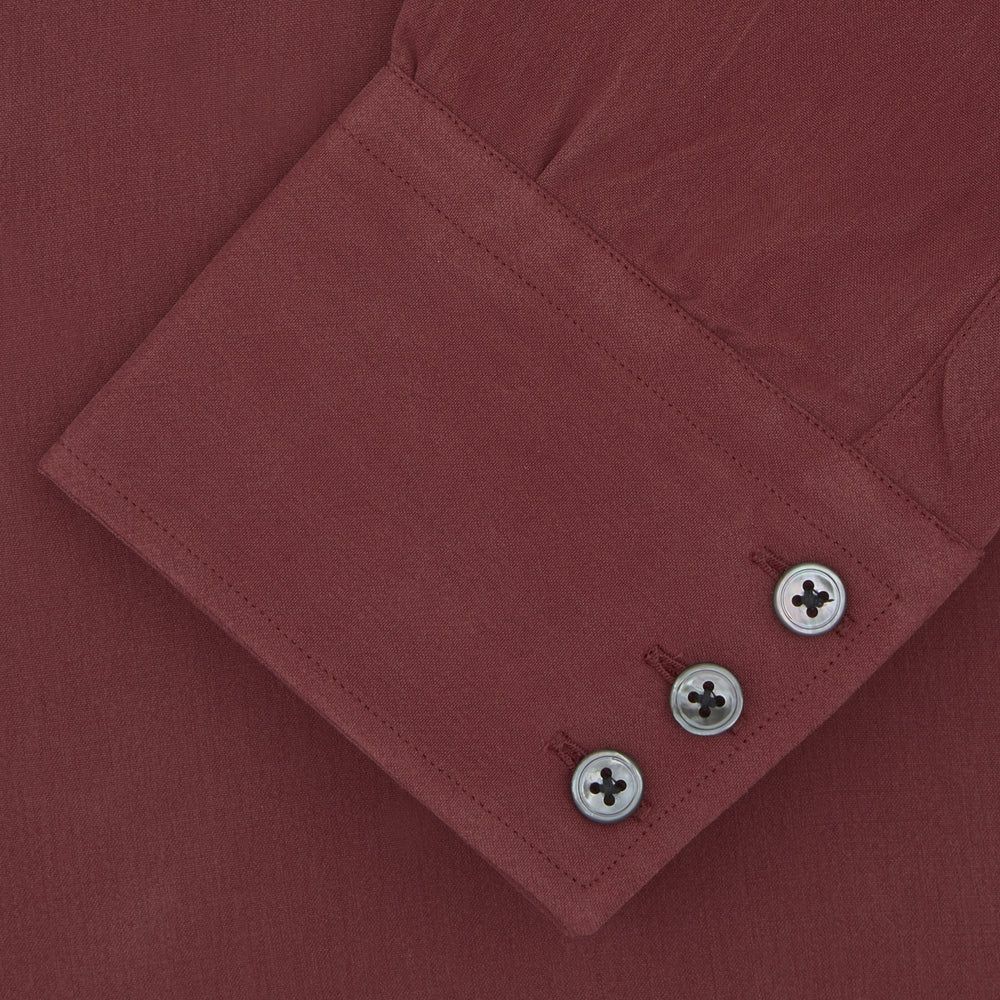 The Turnbull & Asser Burgundy Silk Shirt features a T&A collar and 3-button cuffs, offering a refined alternative to a black tie for modern style. Displayed folded on a white background.