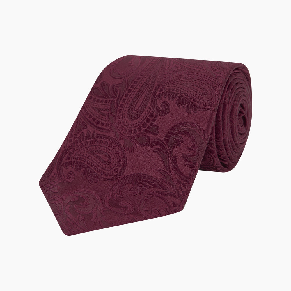 The Turnbull & Asser Burgundy Paisley Silk Tie, showcased rolled on a white background, is an elegant statement piece featuring a refined paisley design for any wardrobe.