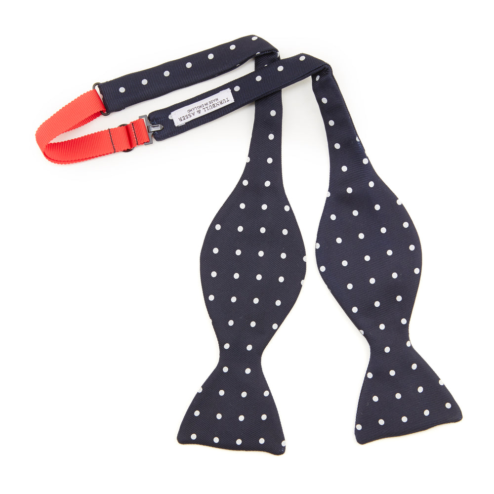 The Winston Navy and White Spot Silk Bow Tie by Turnbull & Asser features classic white polka dots on navy silk, reminiscent of Winston Churchill's style, and is shown against a plain white background.