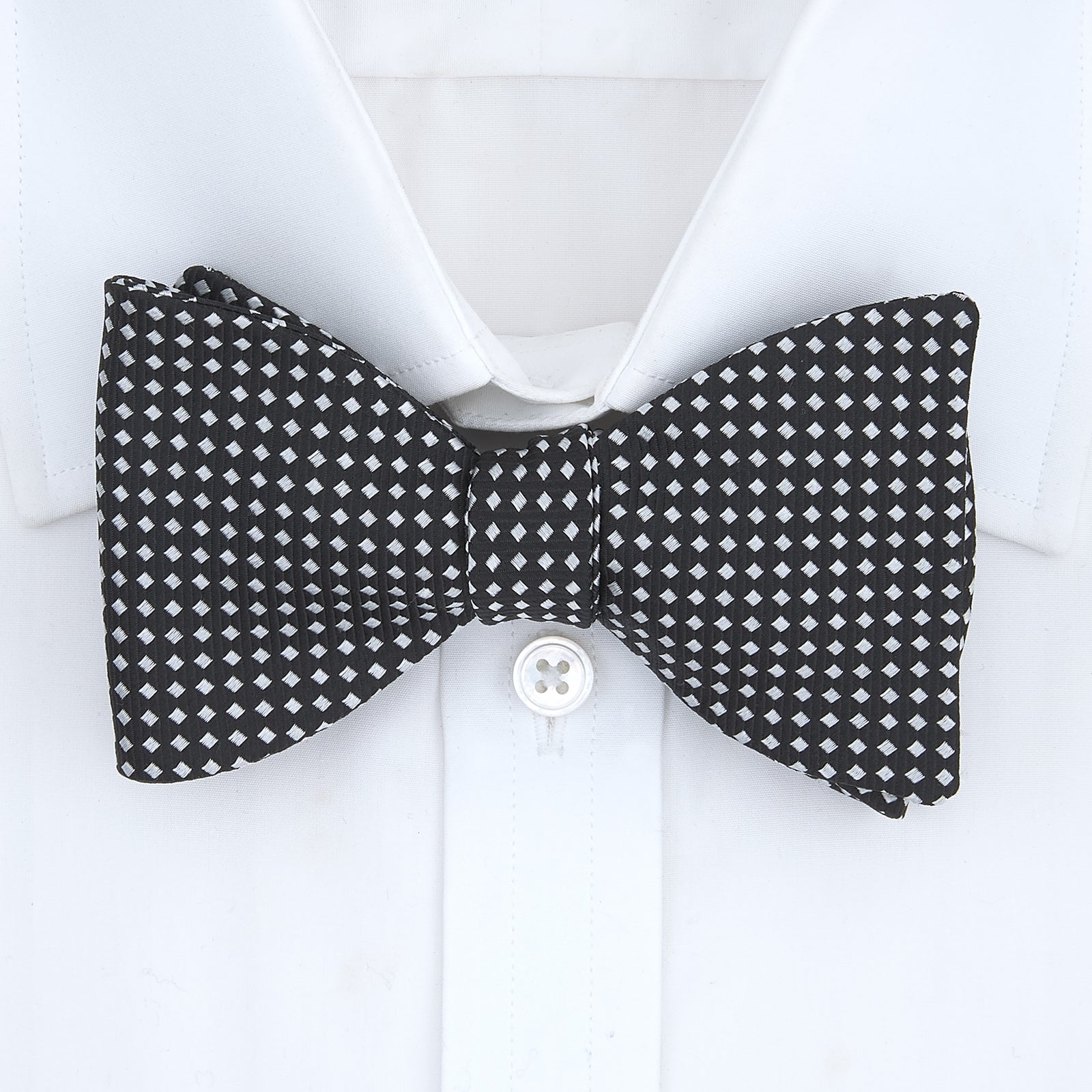 View 2 of product The Turnbull & Asser Diamond Black and White Silk Bow Tie features a black woven silk design with a tessellated diamond pattern of small white shapes, shown against a plain white background.