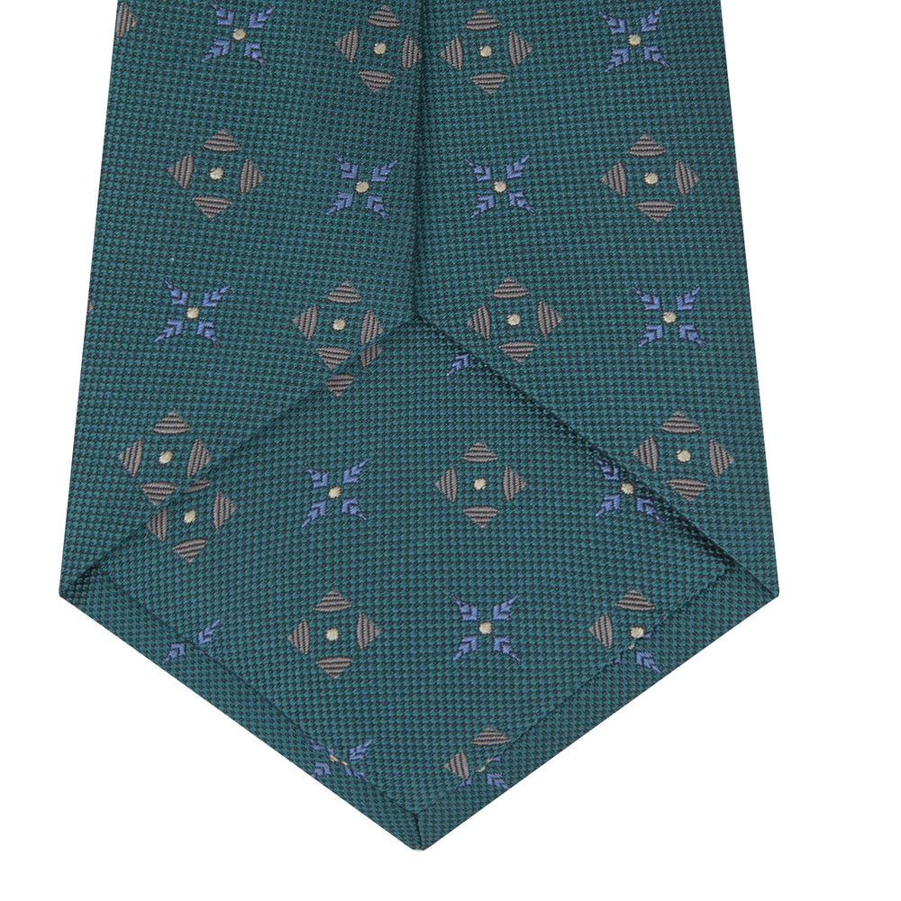 The Turquoise Crosses Silk Tie by Turnbull & Asser features a subtle geometric motif in tan and blue, displayed rolled on a white background—ideal for the modern office.