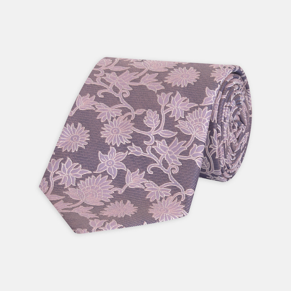 The Turnbull & Asser Pink Floral Occasion Silk Tie features a rolled-up purple jacquard design with a light pink floral pattern, perfect for weddings or floral events, shown on a plain white background.