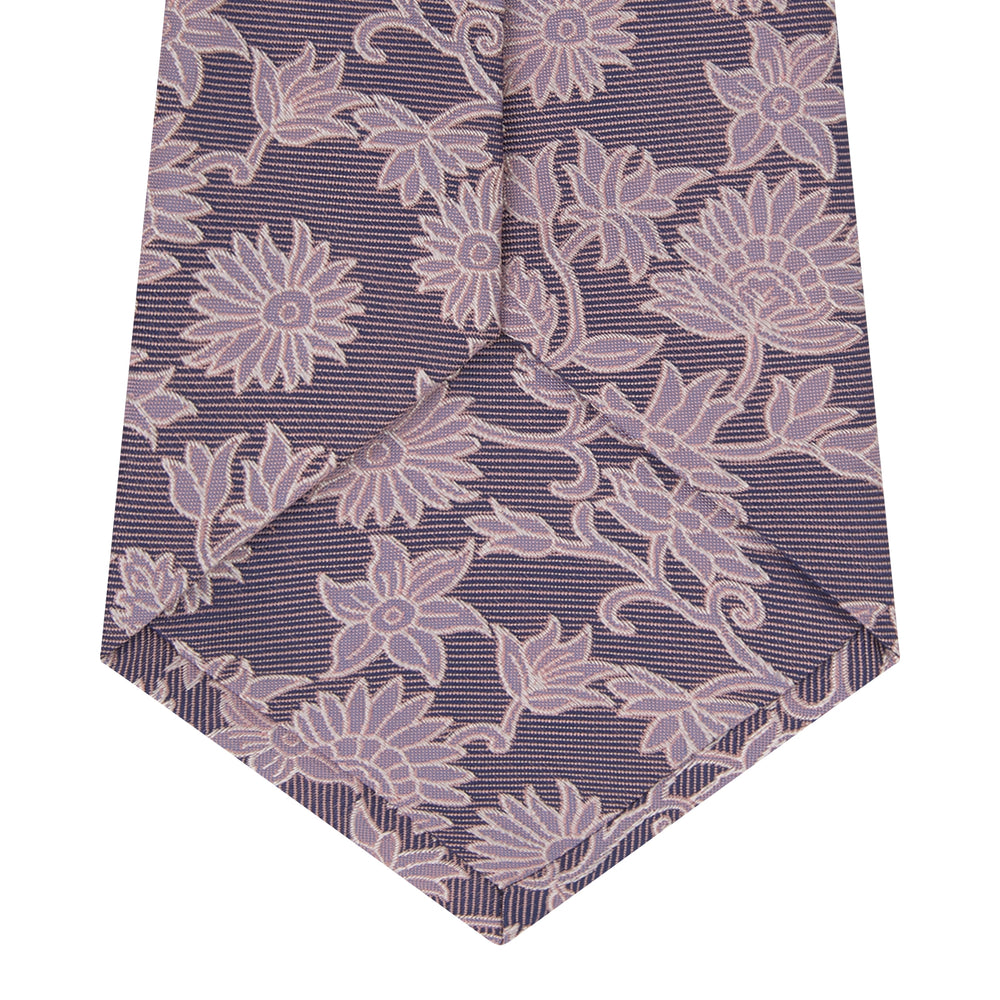 The Turnbull & Asser Pink Floral Occasion Silk Tie features a rolled-up purple jacquard design with a light pink floral pattern, perfect for weddings or floral events, shown on a plain white background.