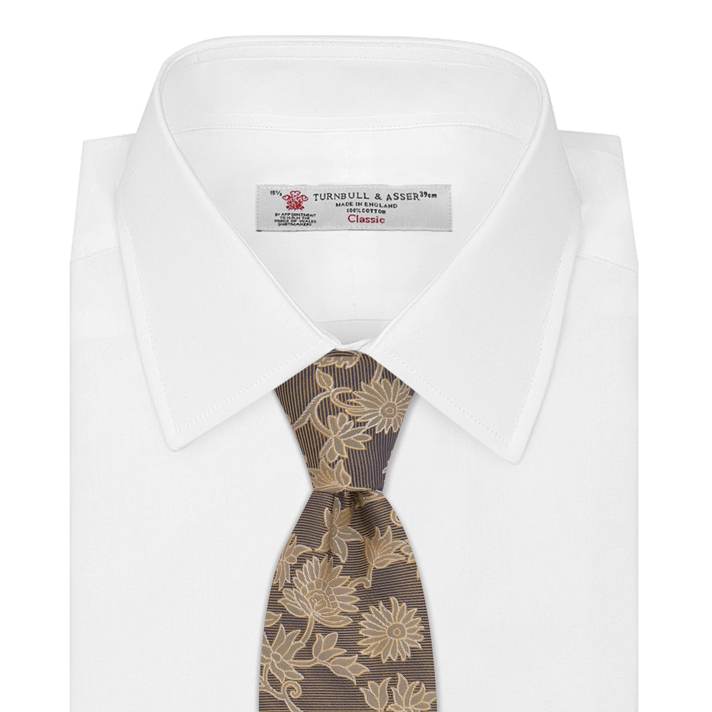 The Copper Floral Occasion Silk Tie by Turnbull & Asser features a gold floral jacquard pattern on brown silk, elegantly rolled on a white surface—an ideal choice for weddings.