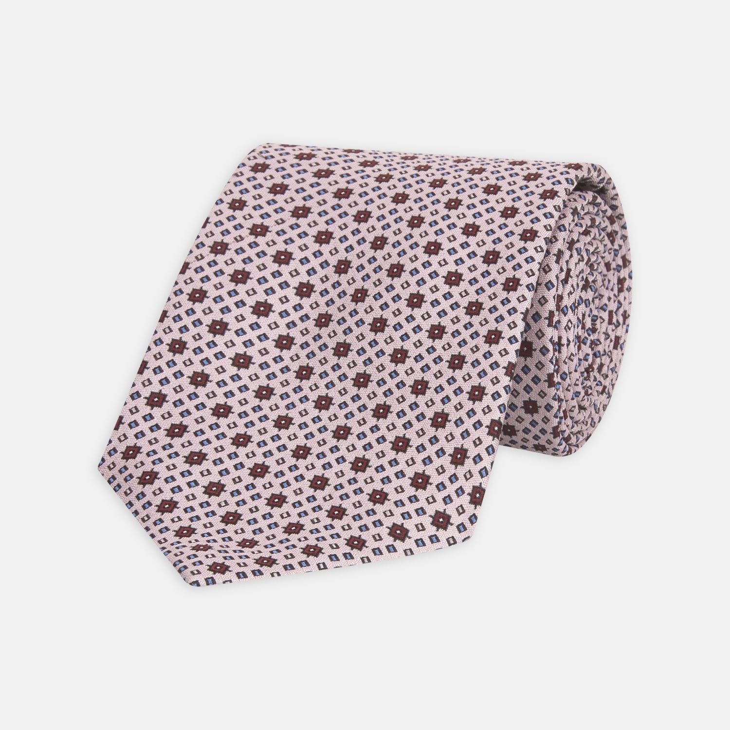 View 1 of product The Turnbull & Asser Pastel Pink Geometric Silk Tie features a small, repeating dark brown and white pattern for a mid-century look—ideal with tailored jackets. Shown rolled up on a white background.