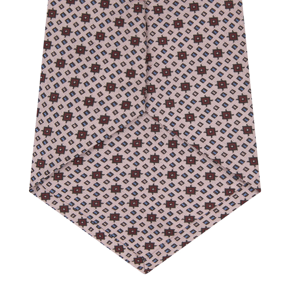 The Turnbull & Asser Pastel Pink Geometric Silk Tie features a small, repeating dark brown and white pattern for a mid-century look—ideal with tailored jackets. Shown rolled up on a white background.