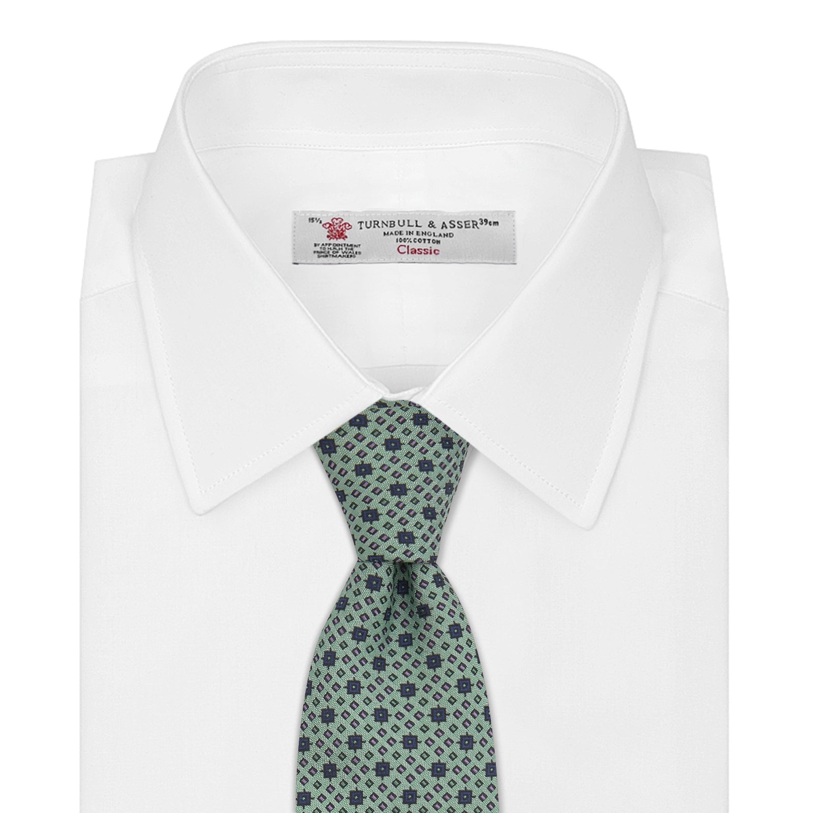 View 2 of product The Leaf Green Geometric Silk Tie by Turnbull & Asser features a repeating pattern of small navy blue and white floral shapes, evoking a mid-century motif. It is neatly rolled and displayed on a white background.
