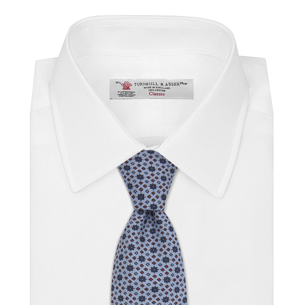 The Turnbull & Asser Sky Blue Geometric Silk Tie features a mid-century dark blue and maroon motif on light blue silk, shown against a white background—ideal for pairing with tailored jackets.