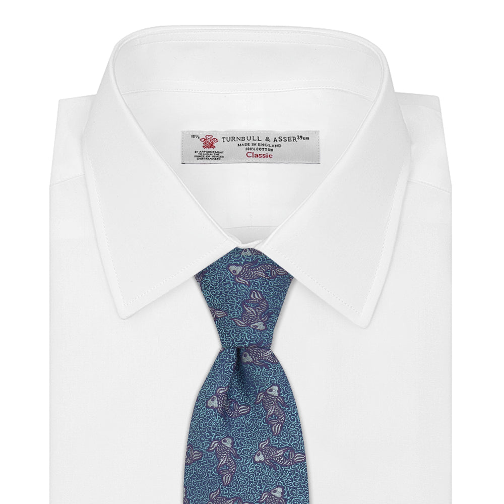 The Turnbull & Asser Turquoise Carp Silk Tie is woven in England, featuring a repeating white and brown carp design on a light blue background with intricate swirling patterns.