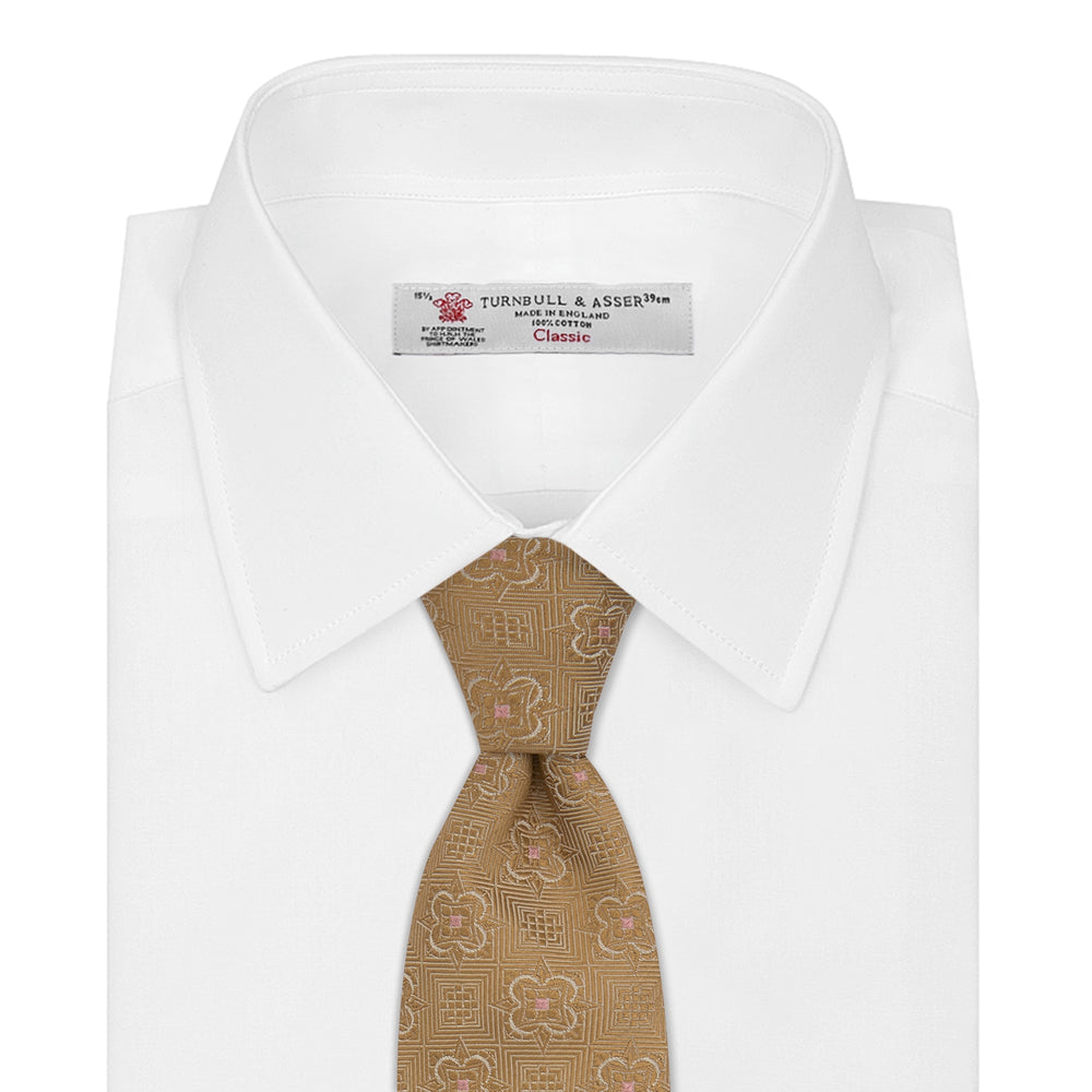The Gold Flower Mosaic Silk Tie by Turnbull & Asser features an intricate gold jacquard pattern of geometric shapes and floral designs in pink and light brown hues.