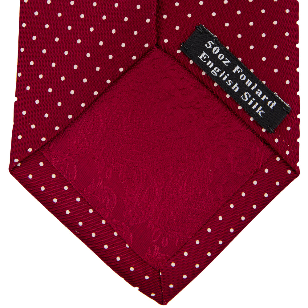 The Turnbull & Asser Burgundy and White Small Spot Printed Silk Tie, shown rolled against a plain white background, is an elegant accessory ideal for the office.